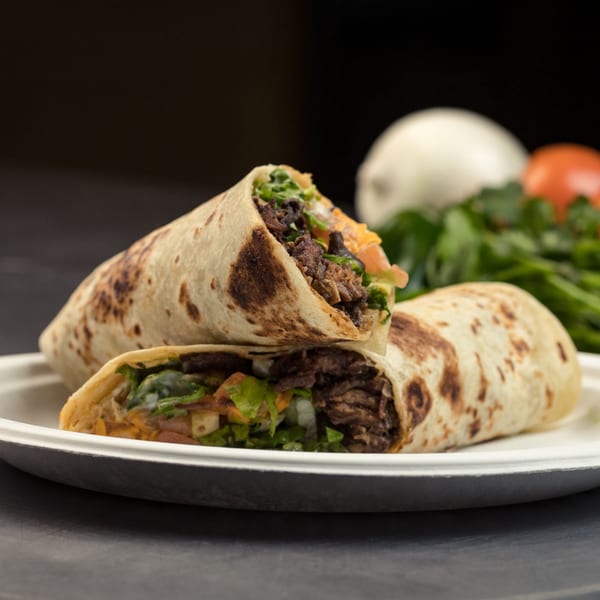 Two Mexican burritos with meat, lettuce, and cheese, on a white plate with vegetables in the background.