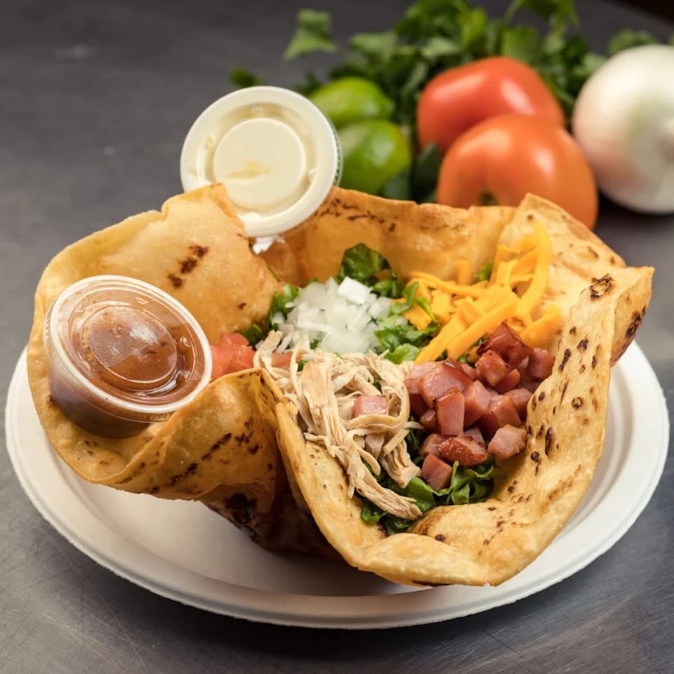 A taco salad in a crispy tortilla bowl with chicken, ham, cheese, and salsa.