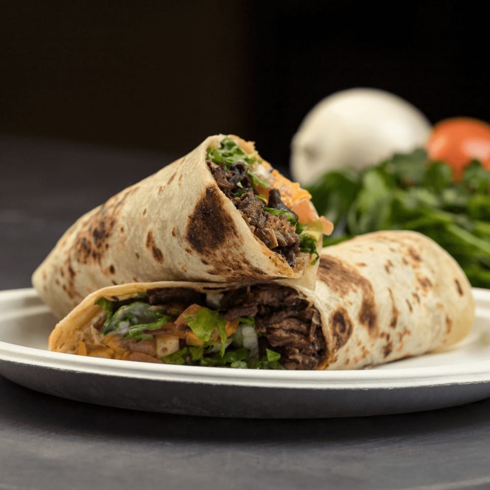 Two Go Burger burritos, filled with meat, lettuce, and cheese, on a white plate with vegetables in the background.