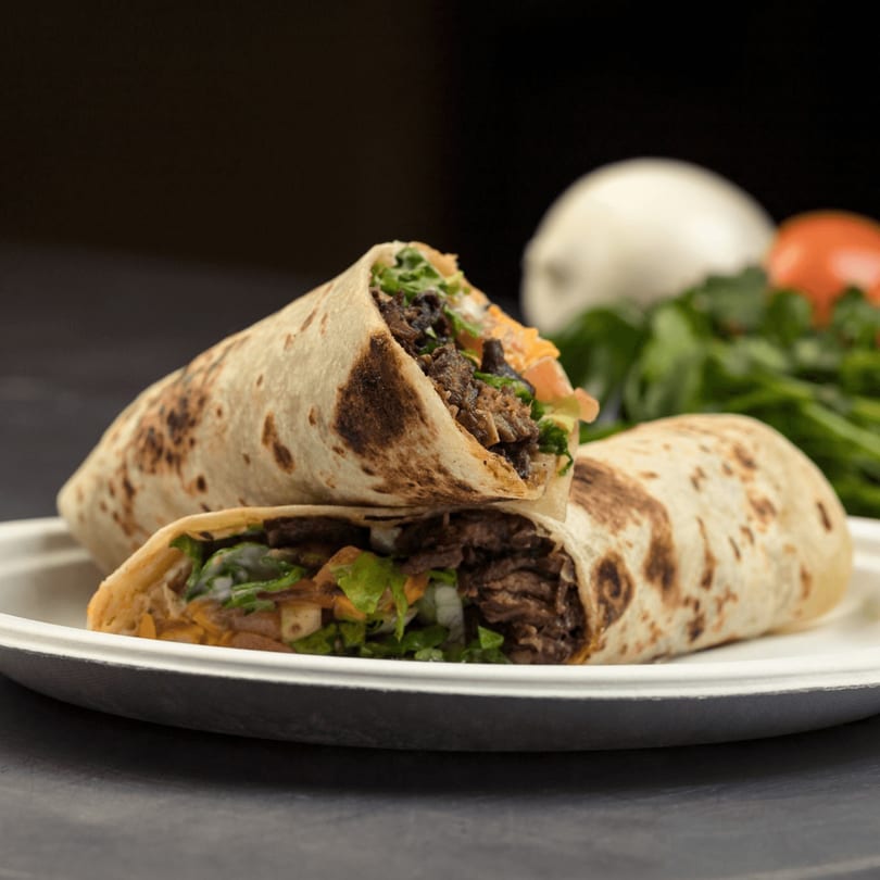 Two Go Burger burritos, filled with meat, lettuce, and cheese, on a white plate with vegetables in the background.